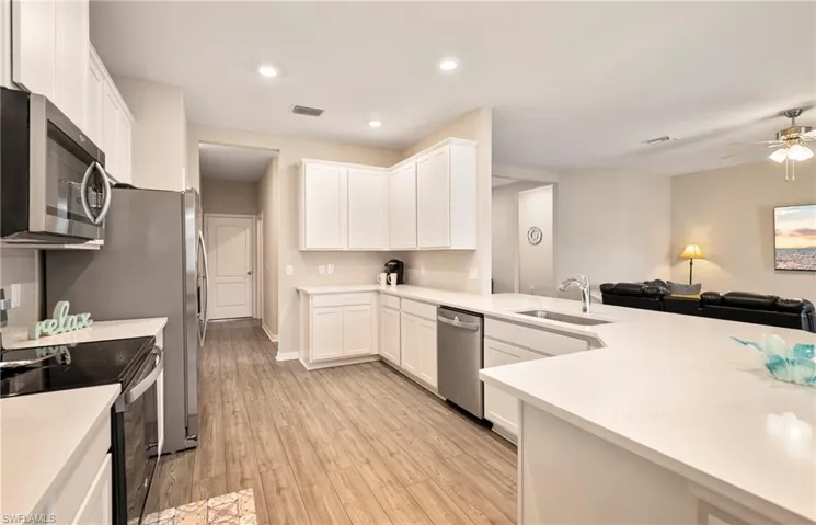 Kitchen with stainless steel appliances, white cabinetry, open floor plan, ceiling fan, and light wood-style flooring