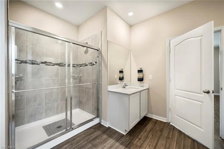 Full bath featuring vanity, a shower stall, dark wood-style floors, and recessed lighting