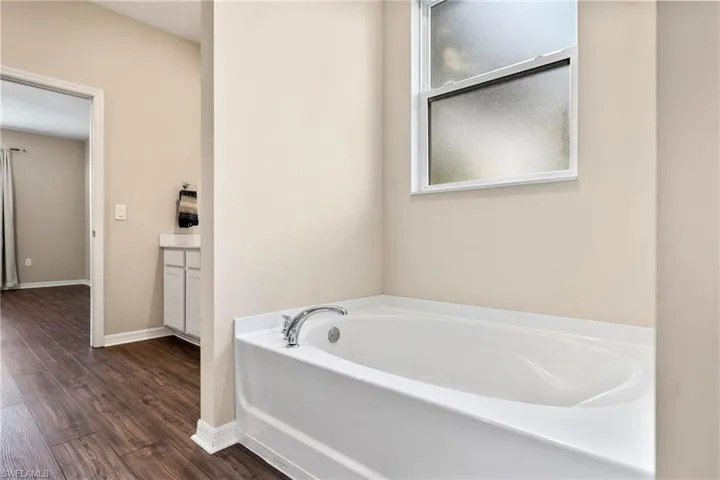 Bathroom with vanity, a bath, and dark wood-style flooring