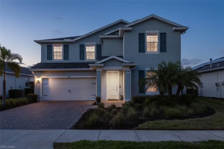 Traditional-style home with an attached garage, decorative driveway, and stucco siding