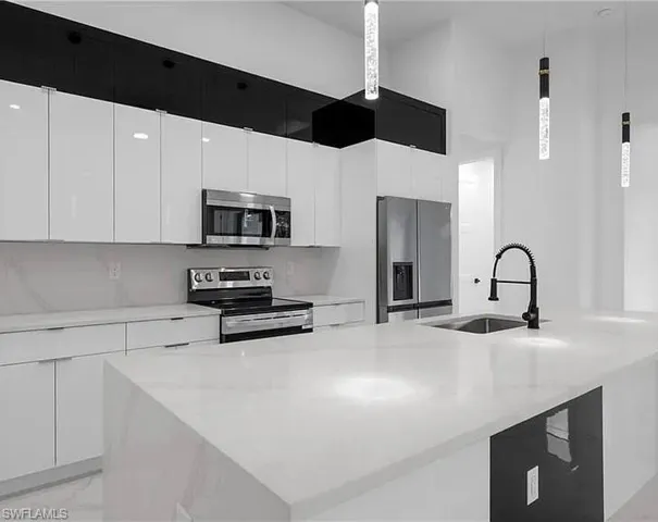 Kitchen featuring stainless steel appliances, a kitchen island with sink, white cabinetry, and light stone countertops