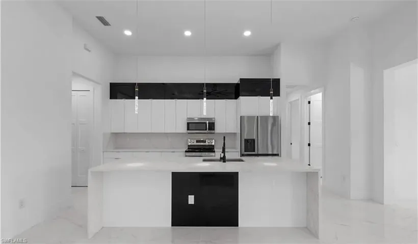 Kitchen featuring stainless steel appliances, a large island, light stone counters, light marble finish flooring, and hanging light fixtures