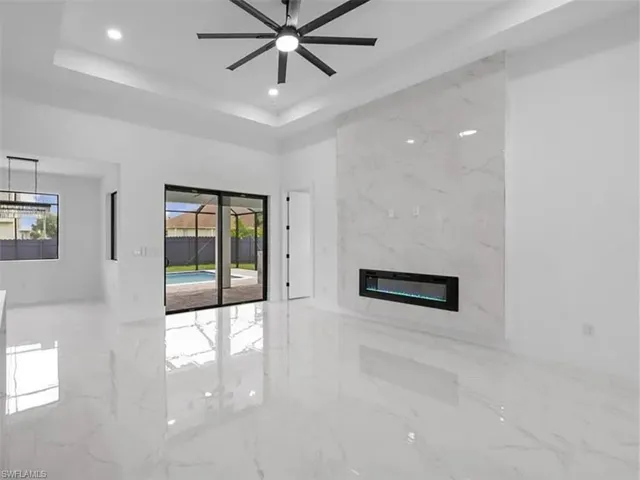 Unfurnished living room with light marble finish flooring, a high end fireplace, a tray ceiling, ceiling fan, and recessed lighting