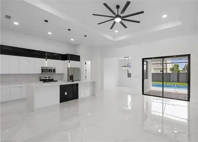 Kitchen with white cabinetry, a large island, a raised ceiling, light marble finish floors, and recessed lighting