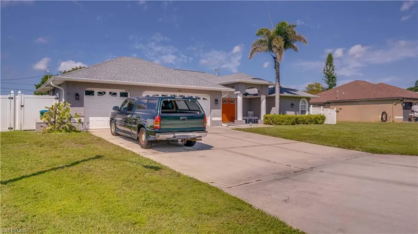 View of front of property with a front yard, a gate, stucco siding, concrete driveway, and a garage