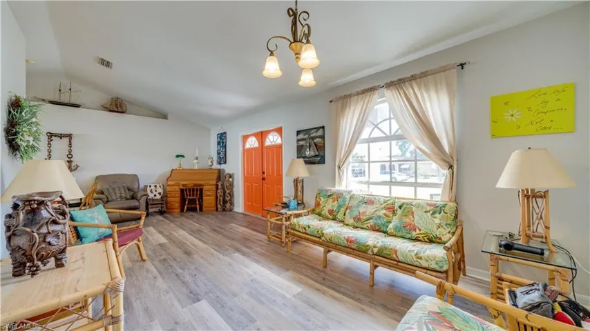 Living room with visible vents, lofted ceiling, wood finished floors, and a chandelier