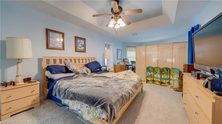Bedroom with visible vents, light colored carpet, a tray ceiling, and ceiling fan