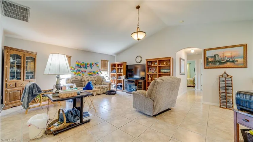 Living area with arched walkways, visible vents, lofted ceiling, and light tile patterned floors