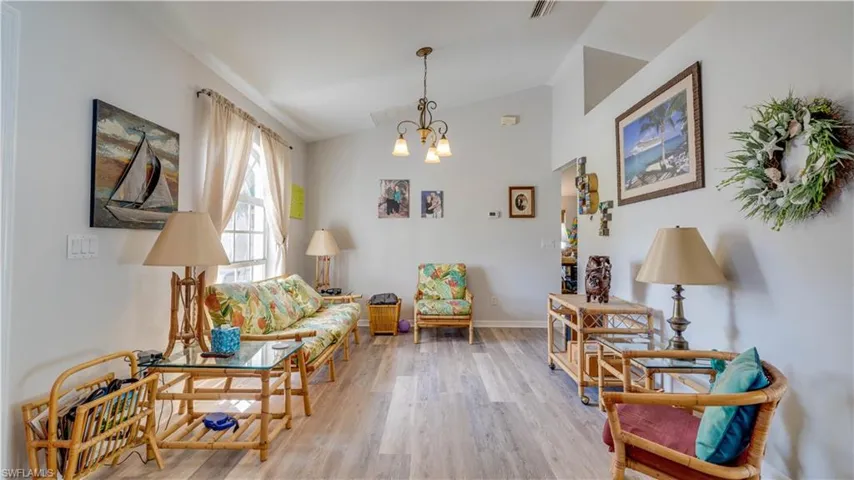 Sitting room with wood finished floors, baseboards, visible vents, vaulted ceiling, and a chandelier