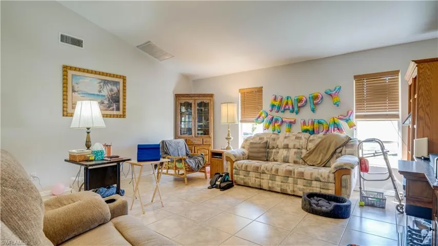 Living room featuring light tile patterned floors, visible vents, baseboards, and lofted ceiling