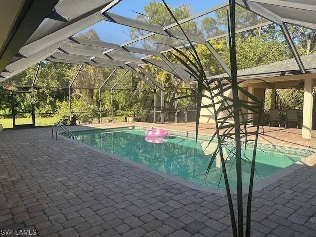 Swimming pool featuring a sunroom, a patio area, glass enclosure, and view of scattered trees