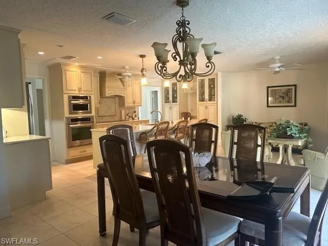 Dining room featuring a chandelier, a textured ceiling, light tile patterned floors, and a ceiling fan