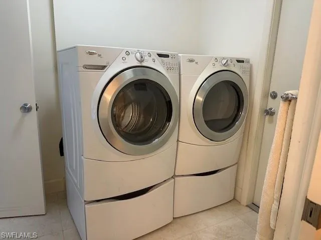 Washroom with washing machine and clothes dryer and light tile patterned flooring