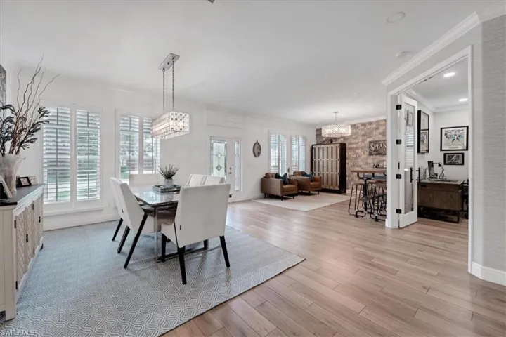 Hardwood-style flooring throughout, with a decorative light fixture above the dining area, plantation shutters on multiple windows, and a brick-finish accent wall
