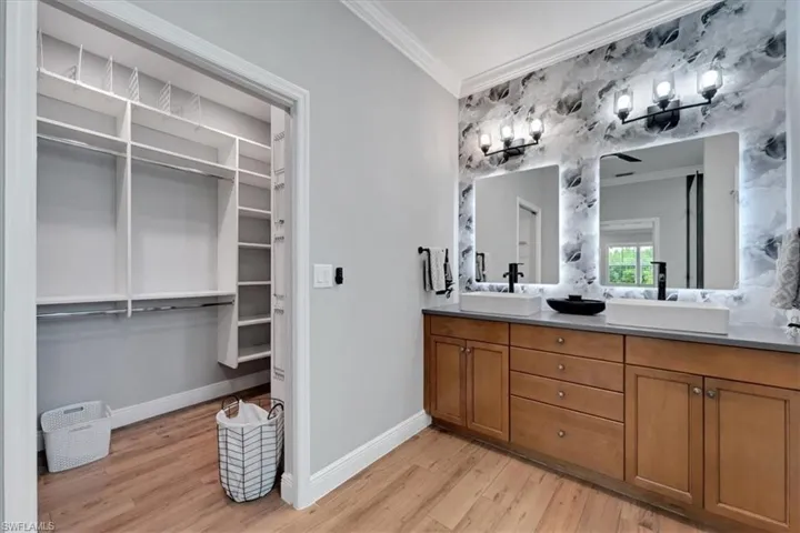Dual vanity featuring wood cabinetry, stone countertop, rectangular vessel sinks, and backlit mirrors