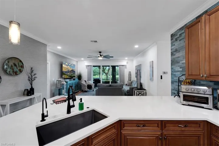 Kitchen island with a black farmhouse sink and matte black faucet, light-toned countertops, wood-finish cabinetry, and a blue tile backsplash