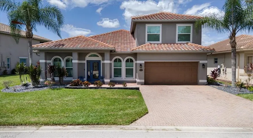 Stucco exterior with a tiled roof, arched windows, and a paver driveway