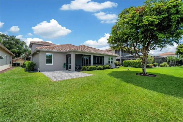 Expansive green lawn featuring a mature tree, an outdoor paver patio, screened lanai, and a tile roof