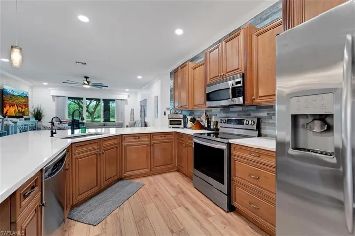 Kitchen featuring wood-finish flooring, stainless steel appliances, white countertops, tile backsplash, and wood cabinetry