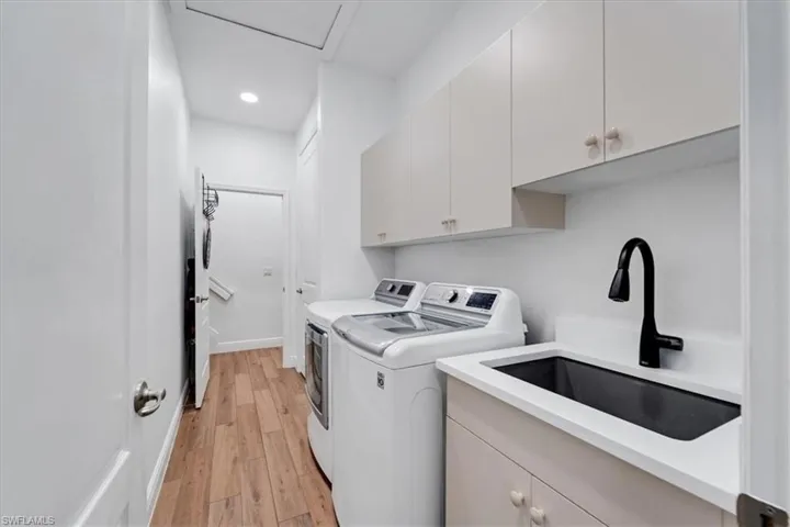 Laundry area featuring wood-finish flooring, white cabinetry, integrated sink, and black gooseneck faucet