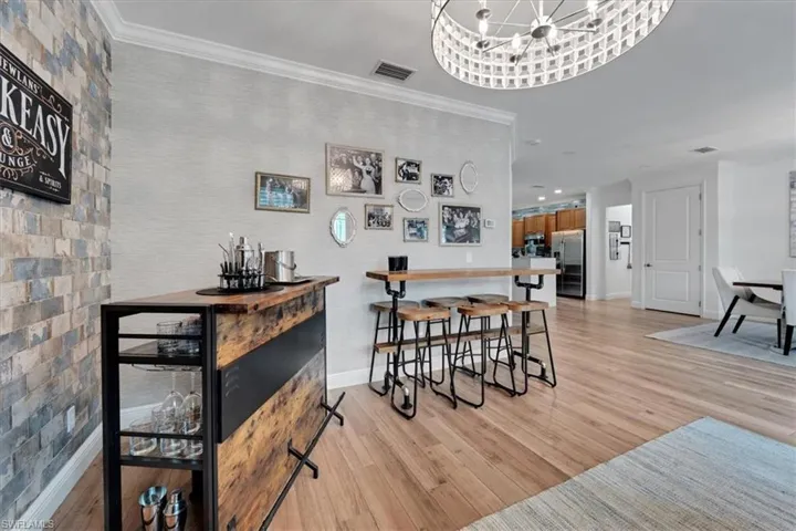 Hardwood-finish flooring, accent wall with stone-look tile, built-in bar area, crown molding, and a unique overhead light fixture