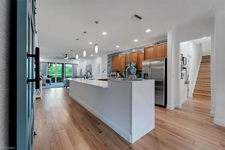 Open-concept living space with wood-finish flooring, a kitchen island, pendant lighting, stainless steel appliances, and a staircase with wood treads