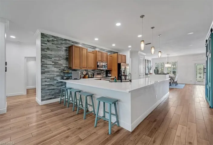 Expansive kitchen island with a light-toned countertop, wood-finish flooring, and pendant lighting