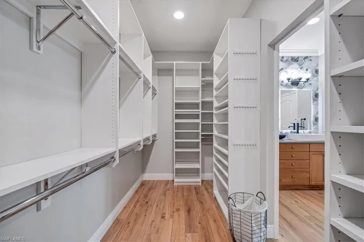 White custom closet system with varied shelving and hanging rods, wood-finish flooring, and recessed lighting
