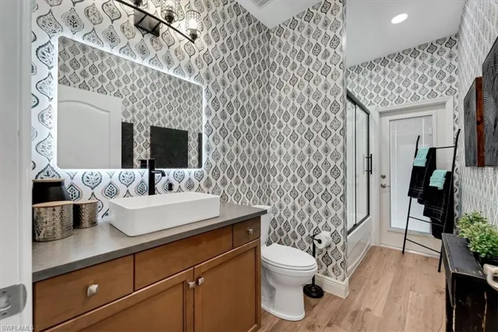 Modern bathroom featuring a rectangular vessel sink with a matte black faucet, illuminated mirror, and wood-finish flooring