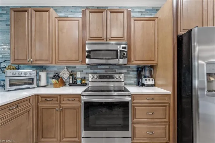 Stainless steel appliances, light wood-finish cabinetry, white countertops, and a blue tile backsplash