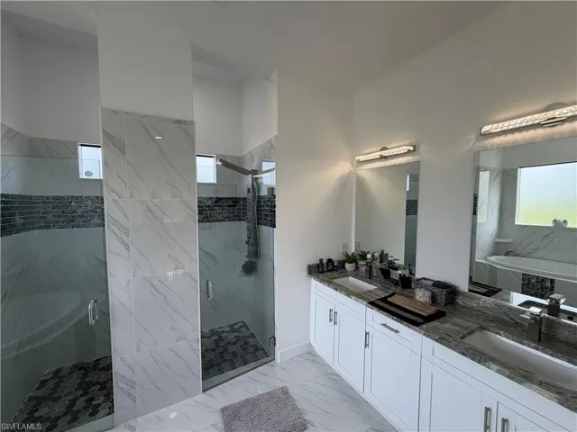 Bathroom with a marble finish shower, double vanity, a bath, and light marble finish flooring