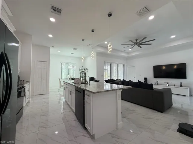 Kitchen featuring white cabinetry, light stone countertops, hanging light fixtures, black appliances, and recessed lighting