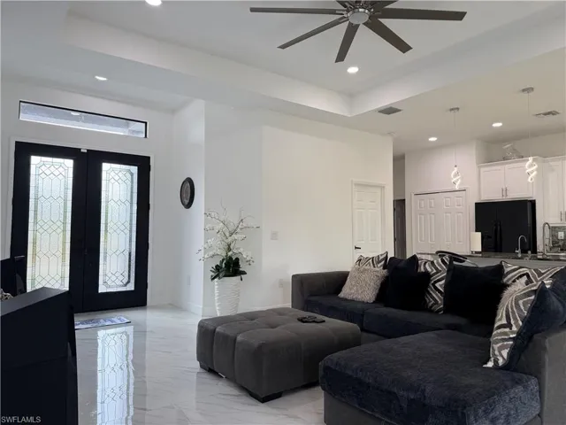 Living area featuring light marble finish flooring, recessed lighting, french doors, ceiling fan, and a tray ceiling