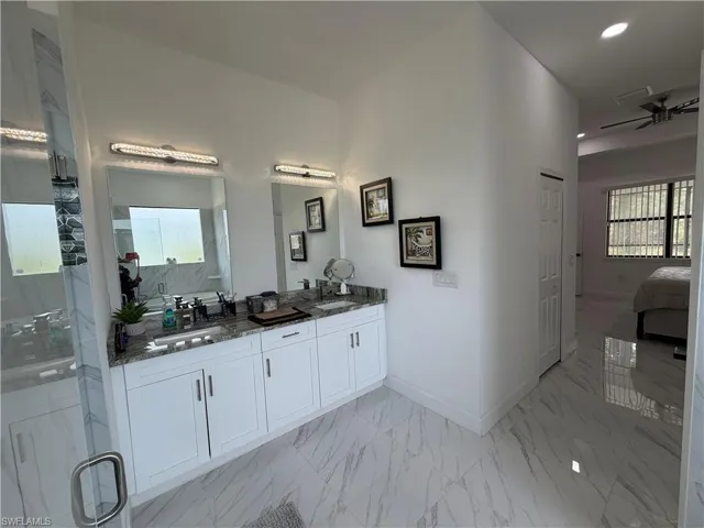 Full bath with double vanity, light marble finish flooring, a marble finish shower, a ceiling fan, and connected bathroom