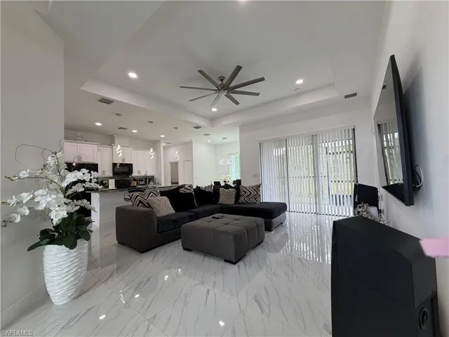 Living area featuring a raised ceiling, light marble finish floors, recessed lighting, and a ceiling fan