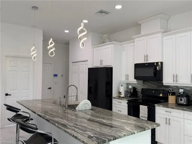 Kitchen featuring dark stone countertops, black appliances, white cabinets, a kitchen island with sink, and recessed lighting