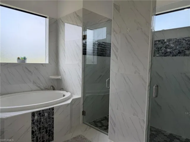 Full bath featuring healthy amount of natural light, a marble finish shower, and a bath