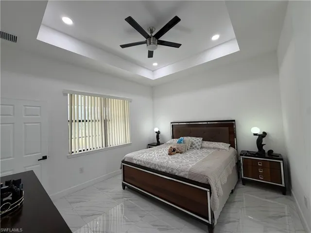Bedroom with a raised ceiling, ceiling fan, light marble finish floors, and recessed lighting