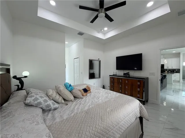 Bedroom with a tray ceiling, light marble finish floors, recessed lighting, a closet, and a ceiling fan