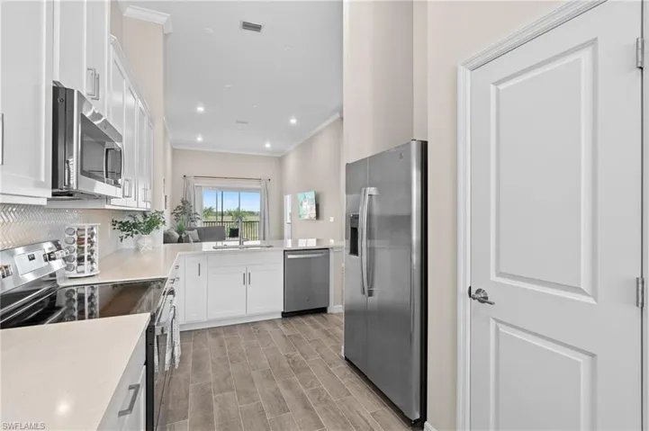 Kitchen featuring white cabinetry, light countertops, ornamental molding, appliances with stainless steel finishes, and backsplash