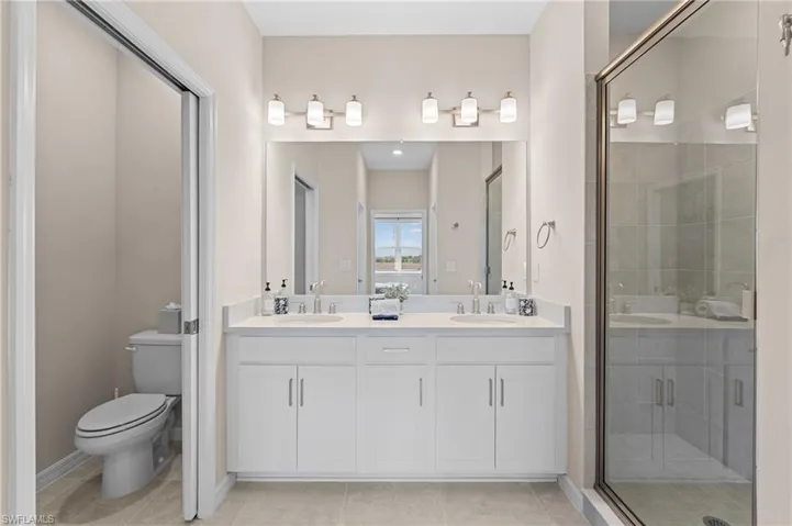 Bathroom with a stall shower, a sink, toilet, and double vanity