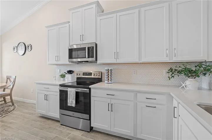 Kitchen featuring stainless steel appliances, light countertops, backsplash, white cabinetry, and a sink