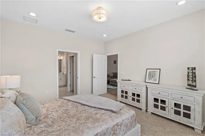 Bedroom with recessed lighting, visible vents, ensuite bathroom, and light colored carpet