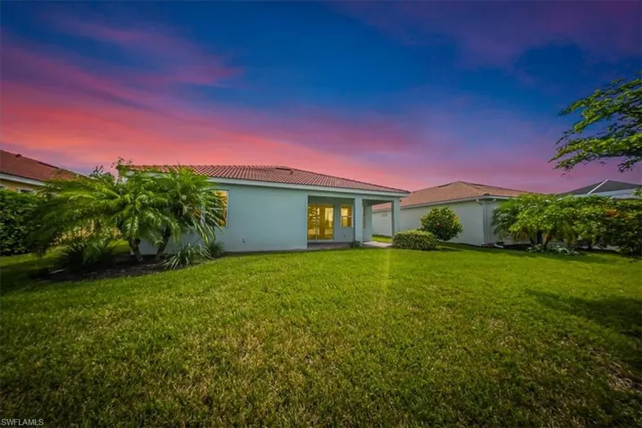 Back of property at dusk featuring a patio area, a yard, stucco siding, and a tile roof