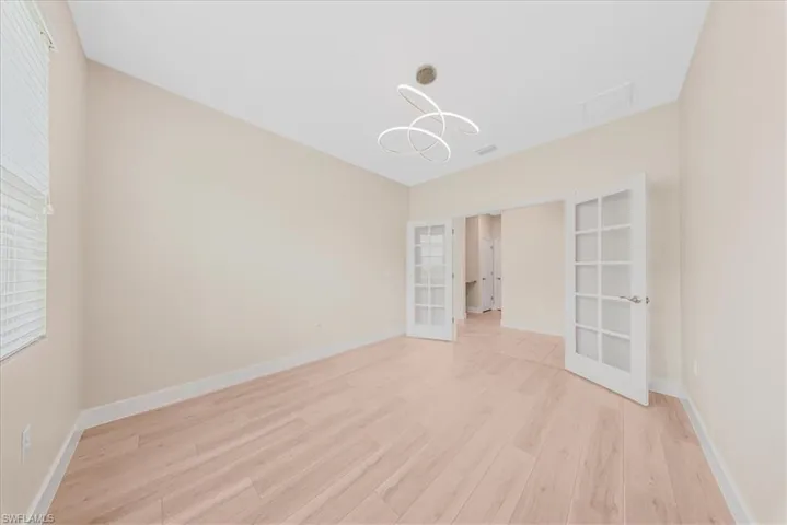 Empty room featuring french doors, light wood-style floors, and a chandelier