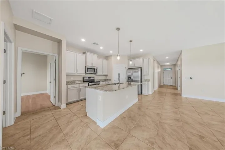 Kitchen featuring decorative light fixtures, a center island with sink, white cabinets, appliances with stainless steel finishes, and light tile patterned floors
