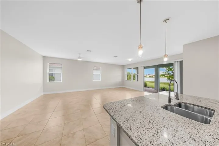 Kitchen with hanging light fixtures, light tile patterned floors, light stone countertops, and open floor plan