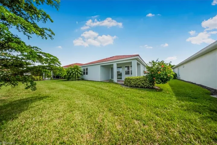 Back of property featuring stucco siding, a lawn, and a tiled roof