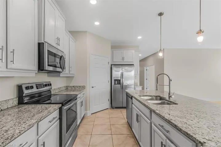 Kitchen with appliances with stainless steel finishes, decorative light fixtures, light stone countertops, light tile patterned floors, and recessed lighting