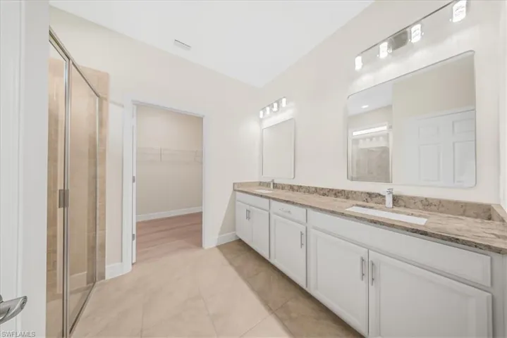 Bathroom with a shower stall, double vanity, a walk in closet, and light tile patterned floors